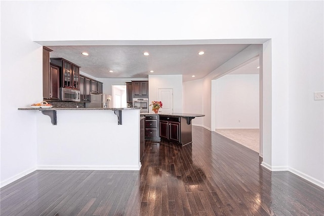 kitchen with a breakfast bar area, stainless steel appliances, a peninsula, dark brown cabinets, and glass insert cabinets