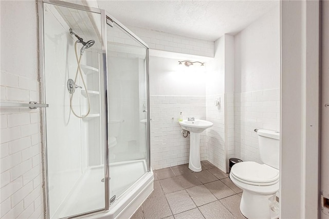 full bathroom with a textured ceiling, tile patterned flooring, toilet, tile walls, and a stall shower