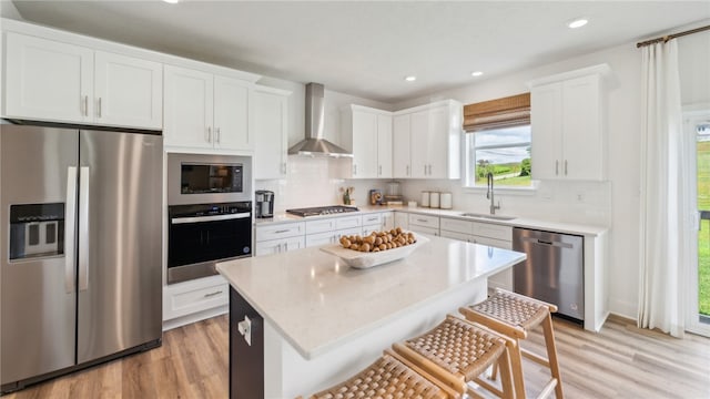 kitchen with stainless steel appliances, a sink, white cabinets, a center island, and wall chimney exhaust hood