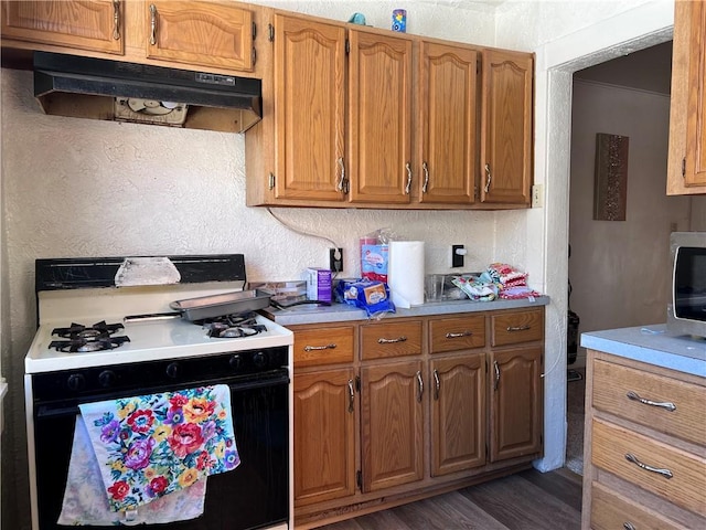 kitchen featuring brown cabinets, gas stove, light countertops, and under cabinet range hood