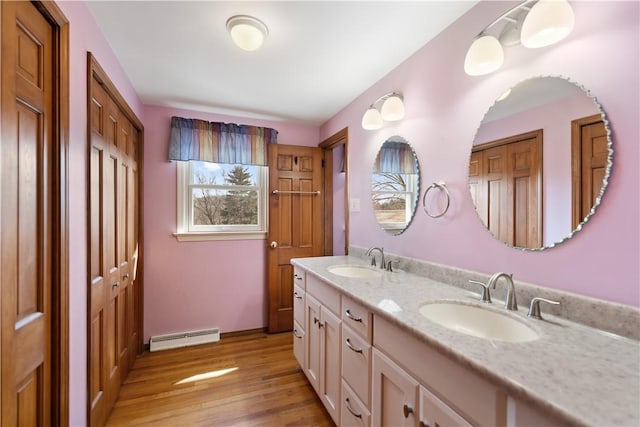 full bathroom featuring double vanity, wood finished floors, baseboard heating, and a sink