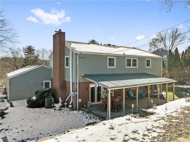 snow covered property with a chimney, cooling unit, and brick siding