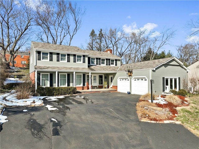 view of front facade featuring brick siding, a chimney, covered porch, a garage, and driveway