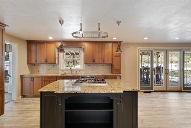 kitchen featuring hanging light fixtures, brown cabinetry, and light stone countertops