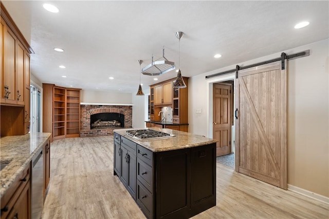 kitchen with a center island, stainless steel appliances, hanging light fixtures, a barn door, and light stone countertops