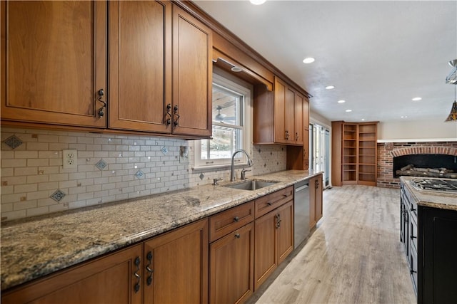 kitchen featuring light wood finished floors, dishwasher, brown cabinets, light stone countertops, and a sink