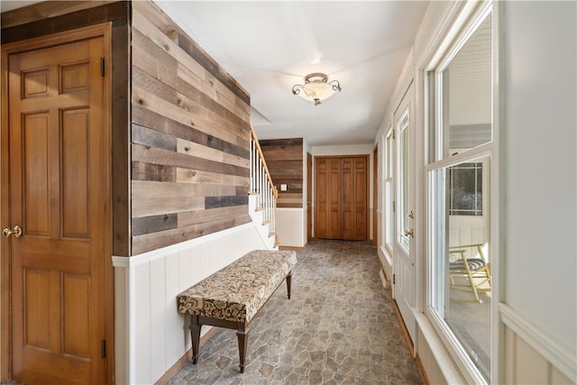 hallway with a wainscoted wall, wood walls, stone finish floor, and stairway