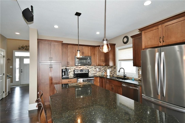 kitchen featuring pendant lighting, brown cabinets, appliances with stainless steel finishes, a sink, and dark stone countertops