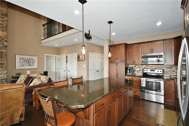 kitchen featuring open floor plan, dark stone countertops, a center island, hanging light fixtures, and stainless steel appliances