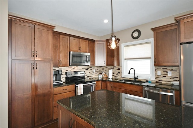 kitchen with brown cabinetry, dark stone counters, stainless steel appliances, pendant lighting, and a sink