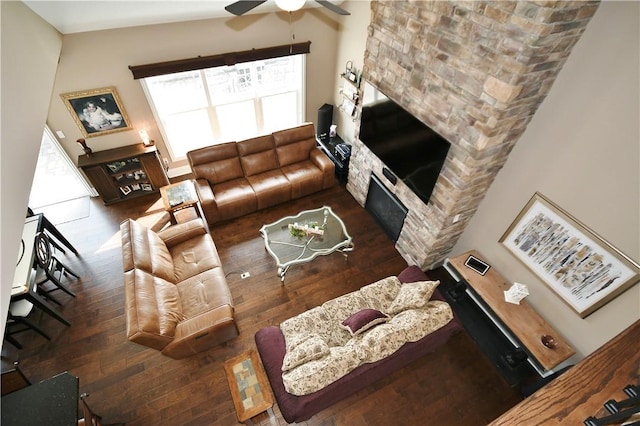 living area featuring a ceiling fan, dark wood finished floors, and a stone fireplace