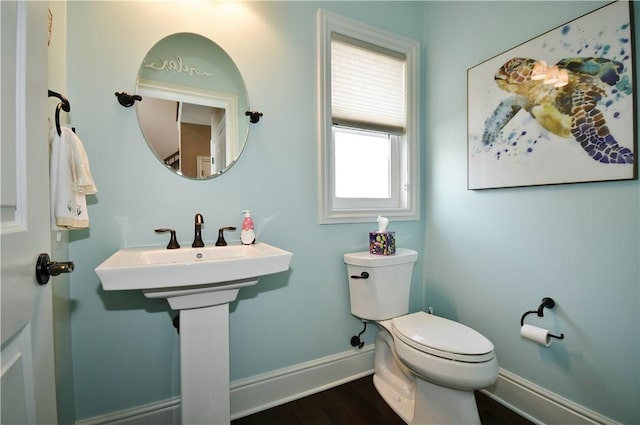 half bath with toilet, baseboards, and wood finished floors