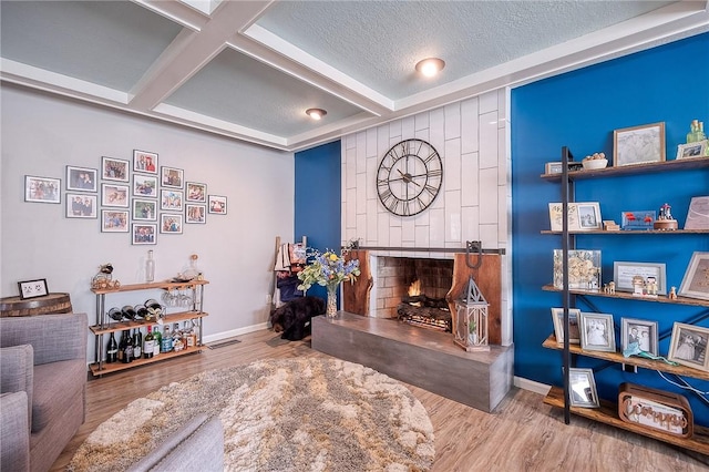 living room featuring a textured ceiling, a fireplace, coffered ceiling, and wood finished floors