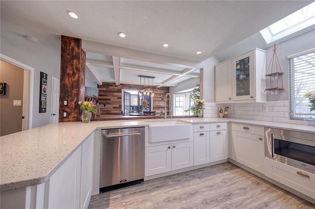 kitchen featuring a peninsula, stainless steel appliances, a sink, white cabinets, and glass insert cabinets