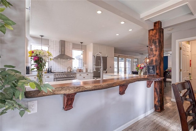 kitchen featuring pendant lighting, white cabinets, wall chimney range hood, a peninsula, and a kitchen breakfast bar