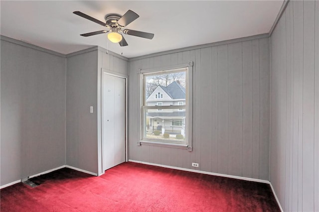 unfurnished room with a ceiling fan, dark colored carpet, and baseboards