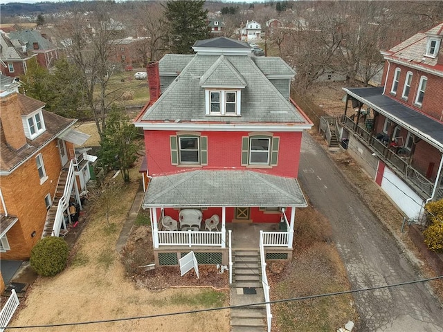 view of front of home with brick siding, a chimney, dirt driveway, covered porch, and stairs