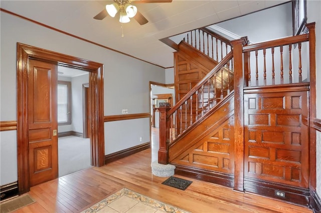 stairway with visible vents, hardwood / wood-style floors, ornamental molding, a ceiling fan, and baseboards