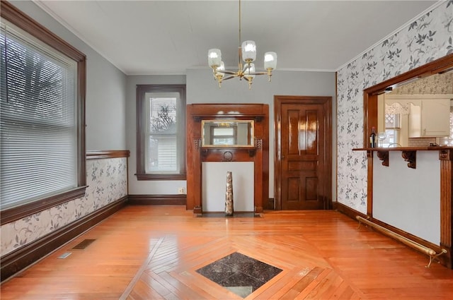 unfurnished dining area featuring crown molding, wallpapered walls, a chandelier, baseboards, and parquet flooring