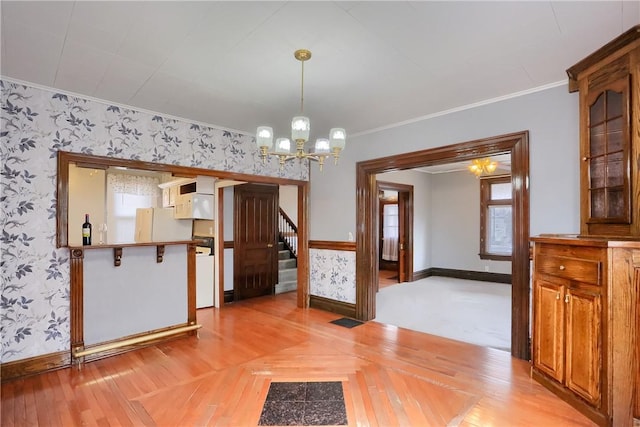 unfurnished dining area with a chandelier, stairway, wainscoting, wallpapered walls, and crown molding