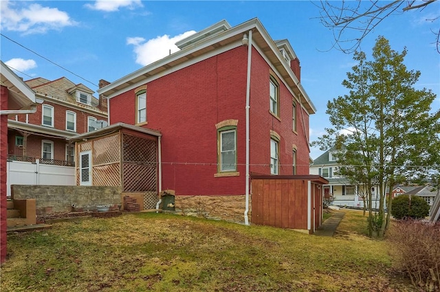 view of side of home featuring brick siding, a lawn, and fence