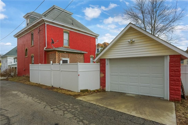 view of property exterior featuring brick siding, an outdoor structure, driveway, and a detached garage