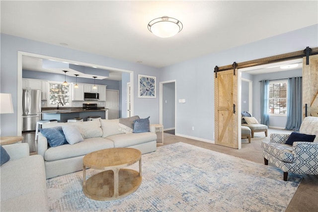 living room featuring light colored carpet, baseboards, and a barn door