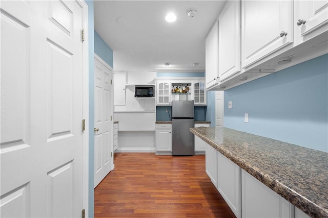 kitchen with black microwave, glass insert cabinets, freestanding refrigerator, and white cabinetry