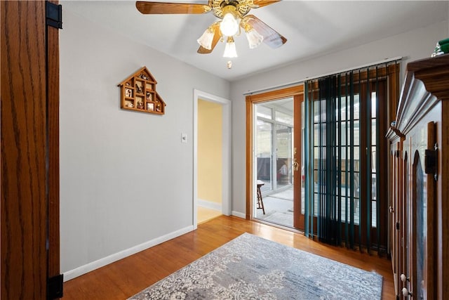 doorway featuring a ceiling fan, baseboards, and wood finished floors