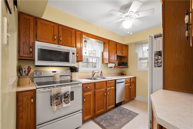 kitchen featuring light countertops, white appliances, a sink, and brown cabinets