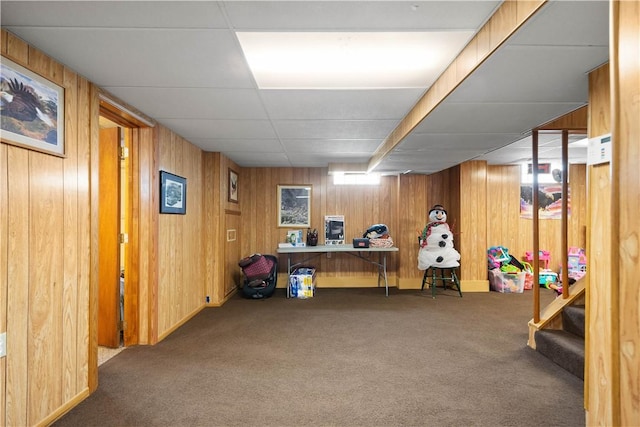 interior space featuring a paneled ceiling, wood walls, and dark colored carpet