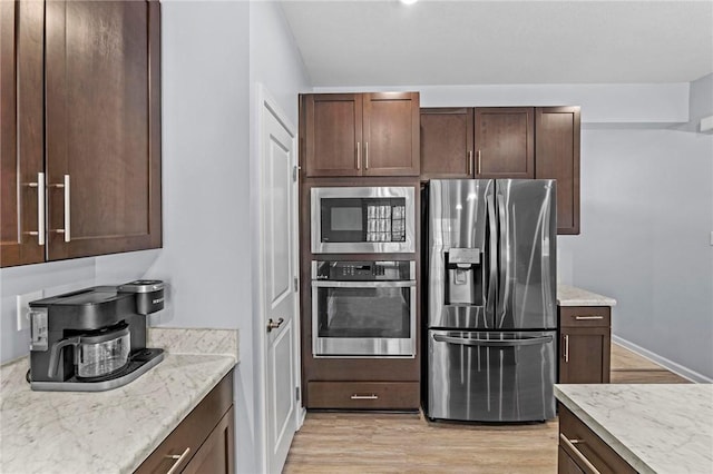 kitchen featuring appliances with stainless steel finishes, light wood-type flooring, dark brown cabinetry, and light stone counters