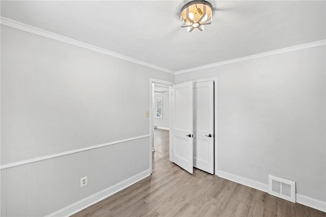 interior space featuring visible vents, baseboards, a wainscoted wall, light wood-style flooring, and crown molding