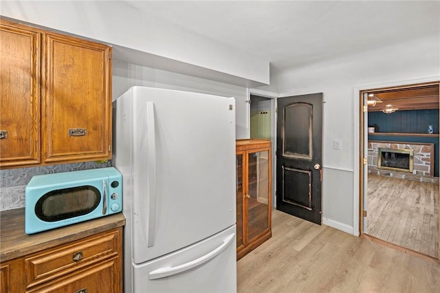 kitchen with light wood-type flooring, a fireplace, brown cabinets, and freestanding refrigerator