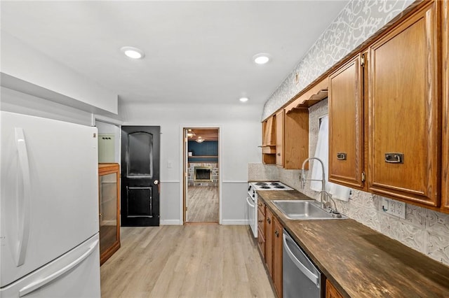 kitchen with white appliances, brown cabinetry, dark countertops, and a sink