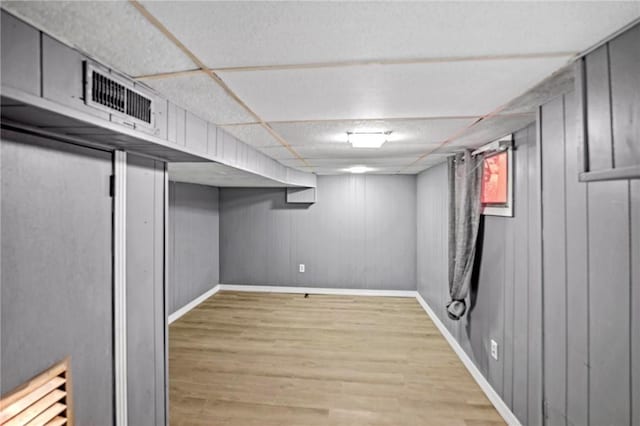 basement featuring light wood-style floors, baseboards, visible vents, and a drop ceiling