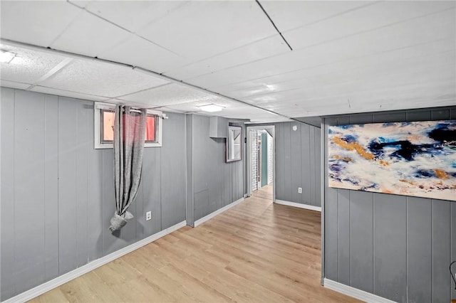 basement with light wood-style flooring, baseboards, and a drop ceiling