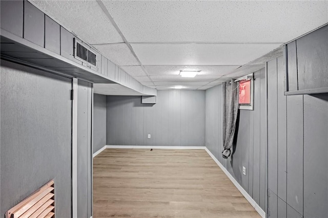 below grade area with a paneled ceiling, visible vents, light wood-style flooring, and baseboards