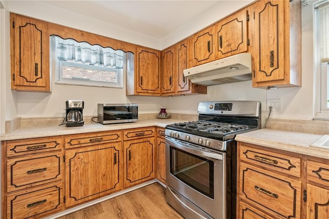 kitchen with brown cabinets, stainless steel appliances, light countertops, light wood-type flooring, and under cabinet range hood