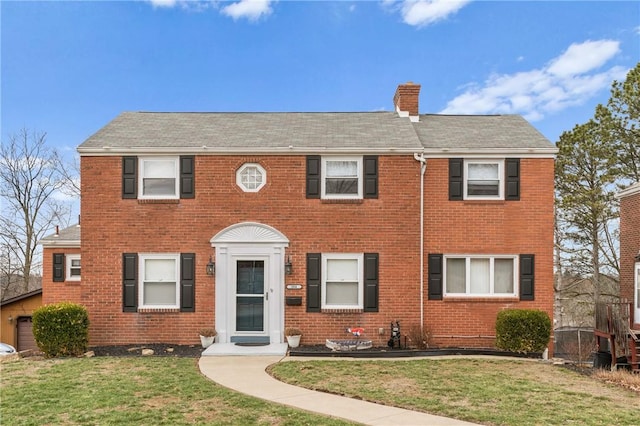 colonial inspired home with a chimney, a front lawn, and brick siding