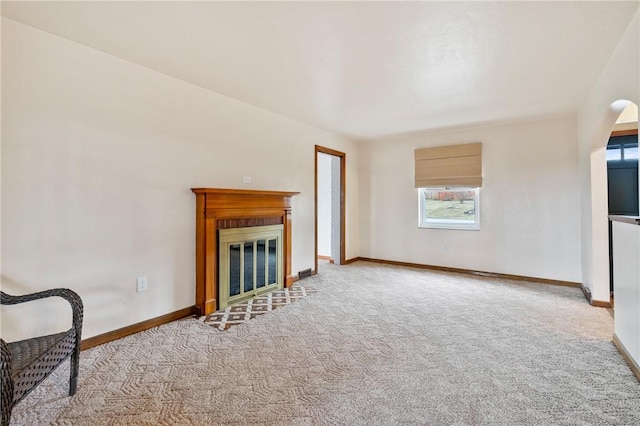 unfurnished living room with baseboards, light colored carpet, arched walkways, and a glass covered fireplace