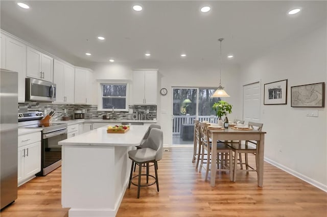 kitchen featuring a center island, decorative light fixtures, stainless steel appliances, light countertops, and white cabinetry