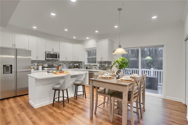 kitchen with a center island, pendant lighting, stainless steel appliances, light countertops, and white cabinets