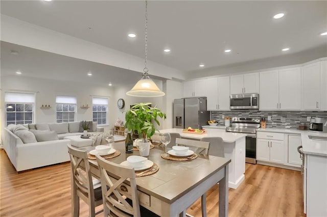 kitchen featuring stainless steel appliances, light countertops, hanging light fixtures, open floor plan, and white cabinets