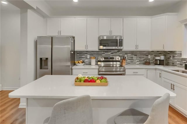 kitchen with stainless steel appliances, a breakfast bar, light countertops, and white cabinetry