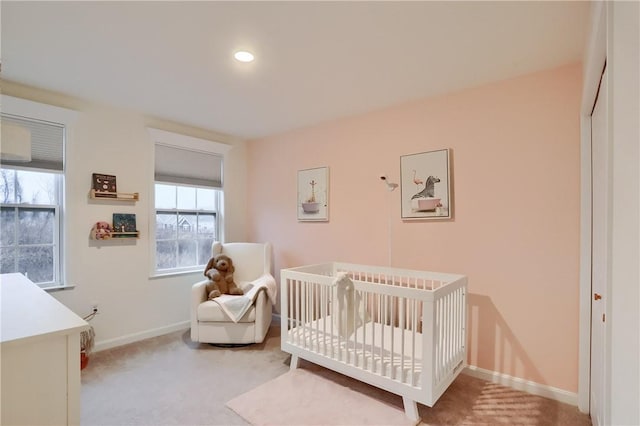 bedroom featuring baseboards, a crib, and light colored carpet