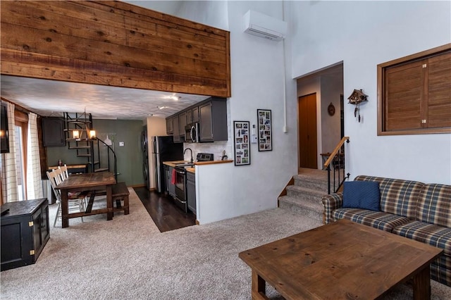 living area featuring a towering ceiling, stairs, an AC wall unit, dark carpet, and an inviting chandelier