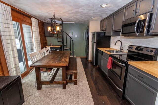 kitchen with stainless steel appliances, wood counters, a sink, tasteful backsplash, and decorative light fixtures