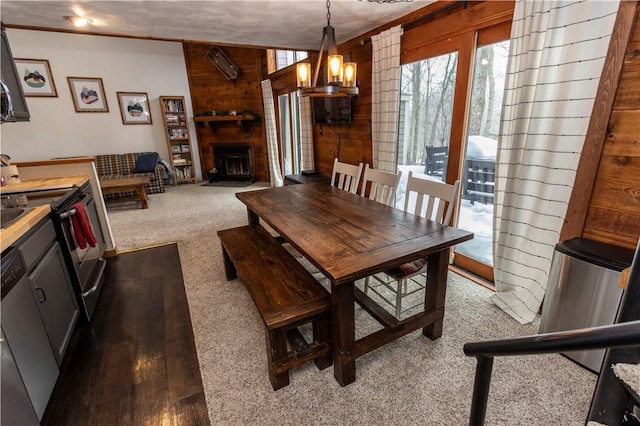 dining area featuring wooden walls, plenty of natural light, a fireplace, and dark colored carpet