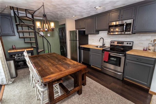 kitchen featuring stainless steel appliances, wood counters, a sink, stacked washer and clothes dryer, and pendant lighting